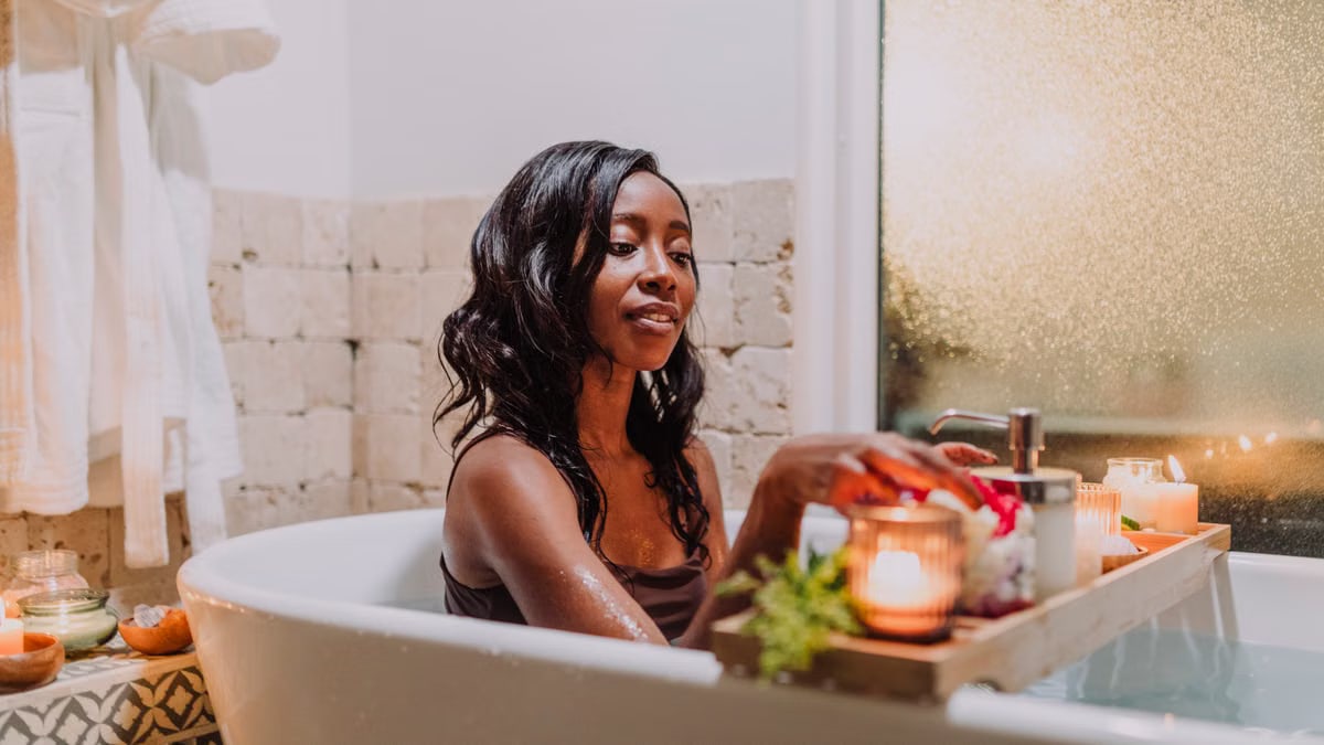 Woman relaxing in a cozy bath with candles and a tray for a calming spa experience.